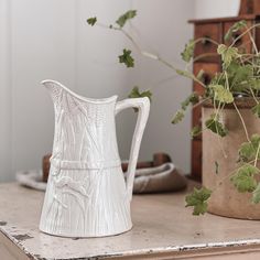 a white vase sitting on top of a table next to a potted green plant