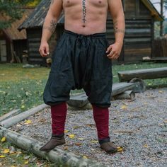 a shirtless man standing in front of a log cabin with tattoos on his chest