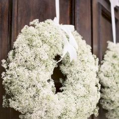 a wreath hanging on the front door of a house with white flowers and ribbon tied around it