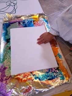 a child is holding a piece of paper and painting on aluminum foil with colorful colors