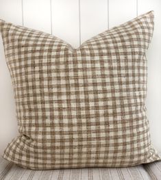 a brown and white checkered pillow sitting on top of a wooden bench next to a wall