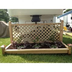 a wooden bench sitting in the grass with flowers growing on it's sides and an rv behind it