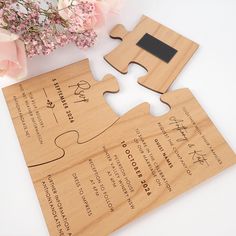 a wooden puzzle piece with two pieces missing from the front and back of it, on top of a table next to pink flowers