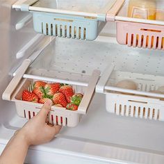 a person reaching into an open refrigerator with some strawberries in the bins on it