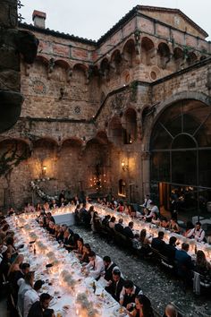 a group of people sitting at tables in front of an old building with lights on