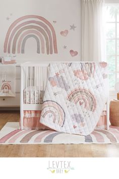 a baby crib with a rainbow wall decal on it and a pink bedding set