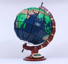 an earth model made out of legos on top of a wooden stand with a white background