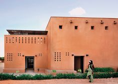 a woman standing in front of a brown building with holes on it's side