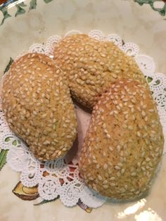 two sesame seed donuts on a plate with doily and paper doily around them