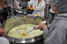 several people are gathered around a large metal pot filled with liquid and whisk