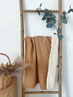 a towel is hanging on a ladder next to a basket with leaves and a plant