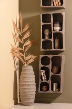 a vase with some plants in it next to two cement boxes on the wall,