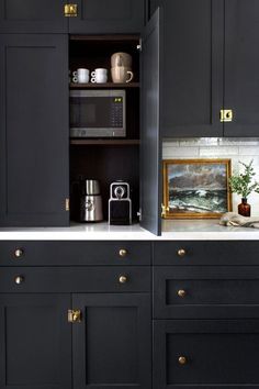 a kitchen with black cabinets and white counter tops, gold pulls on the cupboards