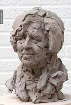 a clay sculpture of a man's head on a wooden table next to a white brick wall