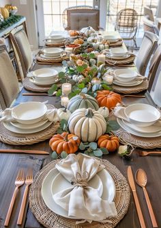 a dining room table set with pumpkins and greenery on the place settings for dinner