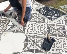 a woman is painting an ornate design on the ground with paint rollers and brush