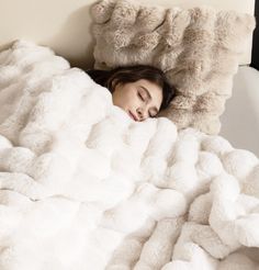 a woman is sleeping under a fluffy white blanket