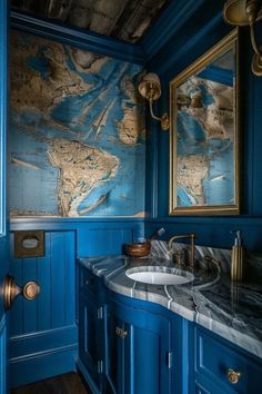 a bathroom with blue walls and marble counter tops, gold faucets and an old world map on the wall