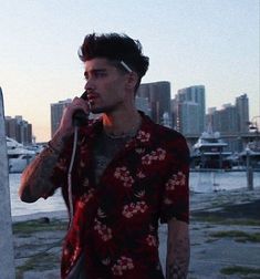 a man with tattoos on his arm talking on a cell phone while standing in front of a body of water