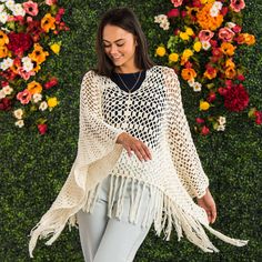 a woman standing in front of flowers wearing a white crochet ponchy