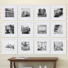 black and white photographs are hung on the wall above a wooden table in front of a shelf