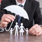 a man holding an umbrella over paper cutouts of two people and a family on a table