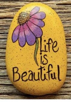 a painted rock with the words life is beautiful written on it and a purple flower