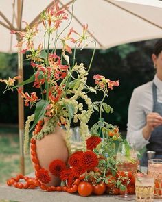 a woman standing next to a table filled with flowers and plants on top of it