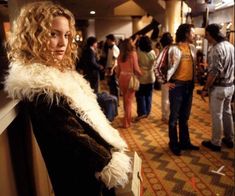 a woman standing next to a group of people in a hallway with luggage on the floor