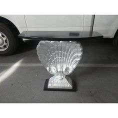 a clear glass vase sitting on top of a black stand next to a white car