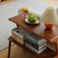 a table topped with books and a bowl of grapes on top of it next to a lamp