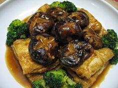 a white plate topped with meat covered in mushrooms and broccoli on top of gravy