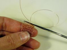 someone is working with some wire to make a ring for the bead on their finger