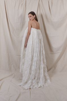 a woman in a white dress is standing against a backdrop with her back turned to the camera