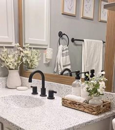 a bathroom sink sitting under a mirror next to a white towel rack with flowers in it