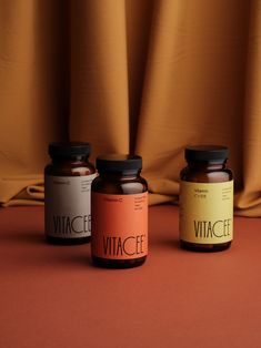 three bottles of vitamins sitting on top of a table next to a brown curtain