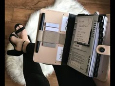 a woman is holding an open planner book in her hand while sitting on the floor