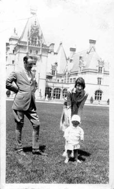 an old black and white photo of two adults and a child in front of a large building