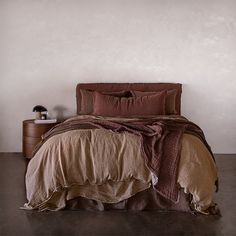 a bed with two pillows and blankets on top of it, next to a night stand