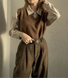 a woman wearing a brown sweater and plaid pants is standing in front of a wall