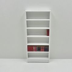 a white book shelf with several books on each shelf and one red book in the middle