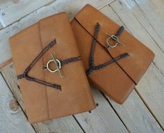 two brown notebooks sitting on top of each other covered in cords and leather straps