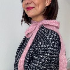 a woman wearing a black and white sweater with a pink scarf around her neck smiling at the camera