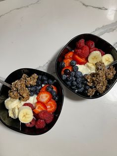 two bowls filled with fruit and granola on top of a white marble countertop