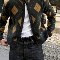 a man standing in the street with his hands on his hips wearing a sweater and jeans