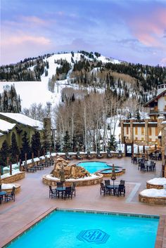 an outdoor swimming pool surrounded by tables and chairs with snow covered mountains in the background