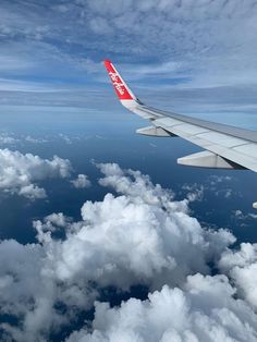 the wing of an airplane flying over clouds in the blue sky with white and red colors