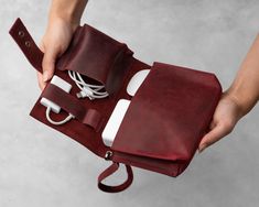 a person is holding a red leather case with cords and charger plugs in it