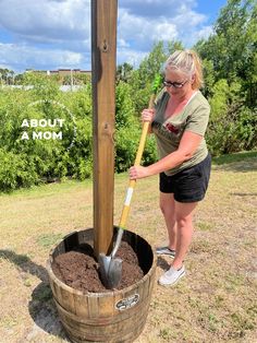 a woman is digging dirt in a barrel with a shovel on the side and a sign above it that says about mom