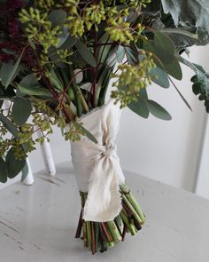 a bouquet of flowers wrapped in burlock tied to a white vase with greenery